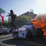 A protester leaps off a burning Waymo taxi near the Metropolitan Detention Center in downtown Los Angeles, Sunday, June 8, 2025, following last night's immigration raid protest. (AP Photo/Eric Thayer)